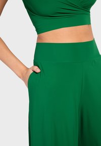 Zeleni skraćeni top i široke hlače od glatke tkanine, s visokim strukom i bočnim džepovima za dodatnu funkcionalnost.