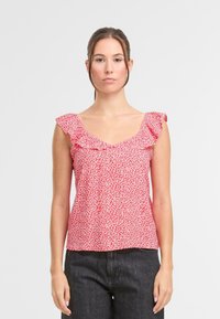 Top senza maniche rosso con spalline a volant, scollatura a V e vestibilità ampia. Il tessuto presenta un piccolo motivo floreale bianco in tutto il capo.