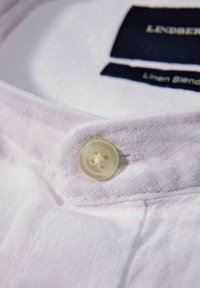 Witte linnenmix overhemdkraag met een opvallend knoopdetail. Textuurstof met zichtbare stiksels en een marineblauw label aan de binnenkant.