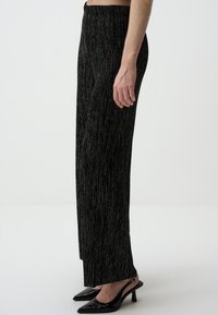 Zwarte, gestructureerde, wijde broek met een subtiele metallic glans, voorzien van een elastische tailleband en rechte pasvorm, gecombineerd met glanzende zwarte hakken.