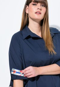 Navyblauwe shirt met een kraag en bloemenpatroon op de manchetten. Glad materiaal met een relaxte pasvorm en een borstzak.