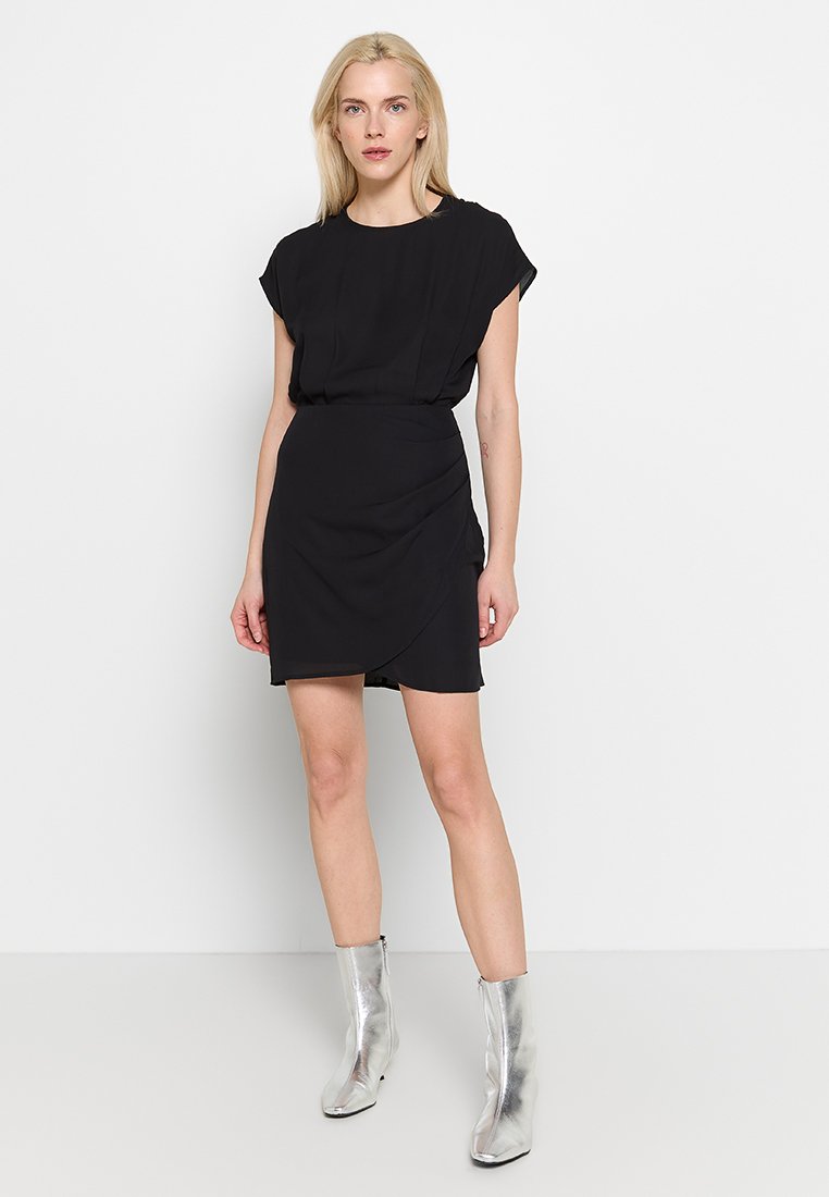 Zwarte jurk met een getailleerde taille, korte mouwen en een wikkelrokdesign. Gecombineerd met glanzende zilveren enkellaarsjes. Eenvoudige, gladde textuur.
