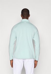 Garas piedurkņu mint zaļš sporta krekls ar rāvējslēdzēja apkakli, bezšuvju pleciem un diskreto logo aizmugurē, izgatavots no gludas, stiepjas auduma.