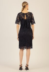 Navy-blaues Spitzenkleid mit kurzen, weiten Ärmeln, einem Schlüssellochausschnitt hinten, taillierter Passform und einem gewellten Saum mit Schlitz für optimale Bewegungsfreiheit.