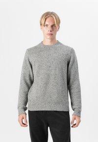 Light gray, textured knit sweater with a round neckline and ribbed cuffs and hem. Paired with dark corduroy pants.