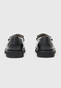 Schwarze Lederschuhe mit flacher Sohle, abgerundeter Spitze und Fersenlasche hinten. Minimalistisches Design mit Nahtdetail entlang der Sohle.