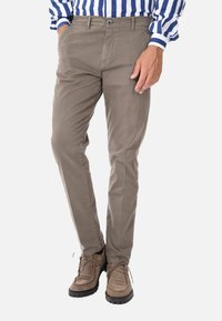 Chinos in cotone beige con vestibilità slim, dotati di tasche laterali, chiusura con bottone e dettagli cuciti nella parte anteriore, abbinati a scarpe marroni con lacci.