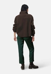 Donkerbruin oversized jack met hoge kraag, gecombineerd met groene corduroy broek. Model draagt bruine enkellaarsjes. Achteraanzicht.