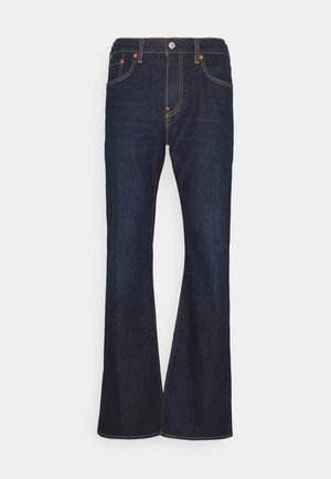 Jean évasé bleu foncé en denim. Il présente un design classique à cinq poches, des coutures dorées et un bouton en métal au niveau de la taille.