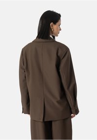 Hnědý přizpůsobený blazer s vykrojeným límcem, zadním rozventováním a manžetami na jedno knoflíček, vyrobený z texturované tkaniny se strukturovaným střihem.