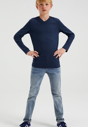 Marinblå långärmad T-shirt med V-hals, tillverkad av mjukt material, kombinerad med ljusblå denimjeans och blå sneakers.