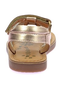 Las sandalias de bronce presentan un diseño de tira metálica con una suela marrón, hebilla ajustable y planta grabada con un motivo floral. Estilo de punta abierta.