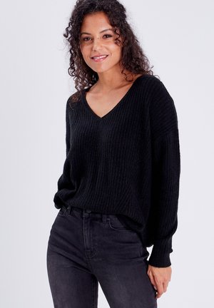 Schwarzer V-Ausschnitt-Pullover mit gerippter Textur, langen Ärmeln und lockerer Passform, kombiniert mit dunklen Jeans. Einfaches und minimales Design.