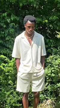Camicetta beige chiaro a maniche corte e pantaloni abbinati, realizzati in un tessuto liscio, con una vestibilità rilassata e colletto a profilo, abbinati a accessori.
