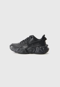 Svart chunky sneakers med bølgete såle, snøring og drageløft bak, vist mot en enkel hvit bakgrunn.