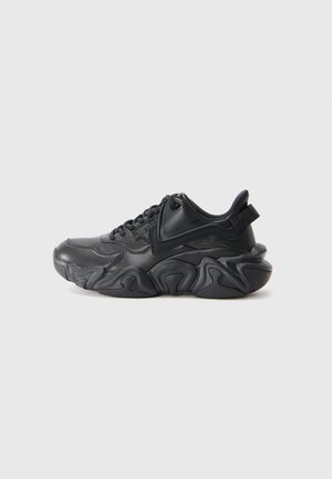 Black chunky sneaker with wave-patterned sole, laces, and pull tab on back, displayed against a plain white background.