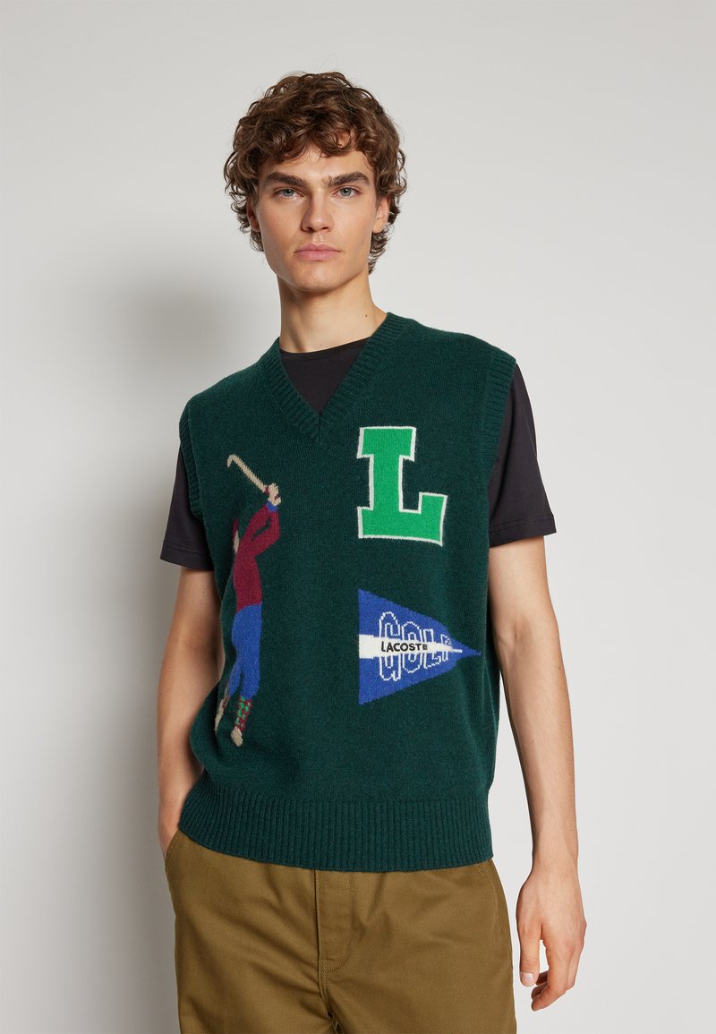 Gilet in maglia verde con scollatura a V, caratterizzato da grafiche colorate legate al golf e dettagli decorativi, tra cui una grande "L" e un logo.