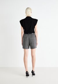 Haut noir à manches courtes avec rembourrage aux épaules, associé à un short gris texturé et des chaussures à talons hauts noires, vu de dos.