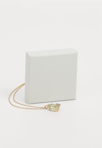 Guld halskæde med en frøformet vedhæng, der har en grøn sten, vist ved siden af en struktureret hvid boks, der viser dens form og design.