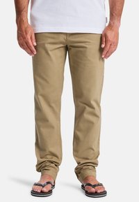 Khaki cotton pants with a straight fit, featuring front pockets and subtle stitching details, paired with black flip-flops.