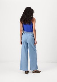 Pantalons larges bleu clair avec une ceinture élastique, associés à un haut sans manches bleu et des chaussures à imprimé animal. Texture de tissu douce.