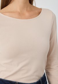 Long-sleeve top in a light beige, soft stretch fabric with a wide neckline, featuring subtle texture and a fitted cut.