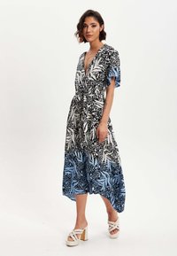 Maxi dress with a deep V-neck, short flutter sleeves, and a tied waist. Features a black and white abstract pattern with blue accents.