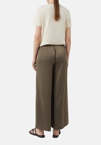 Wide-legged olive green pants, textured fabric, elastic waistband; paired with a short-sleeve light beige top and black sandals.