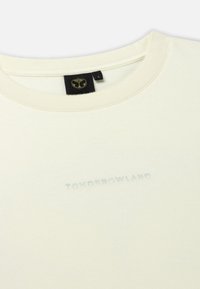 Lichtcreme kleurige katoenen T-shirt met een ronde hals. Voorzien van een subtiele, blauwe, reliëf "TOMORROWLAND" logo. Zachte textuur, eenvoudig ontwerp.