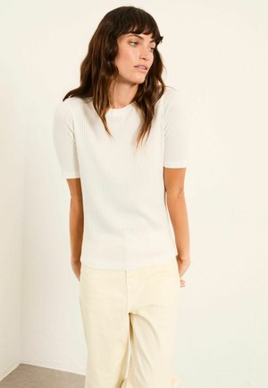 Weißes, geripptes Kurzarmoberteil mit Rundhalsausschnitt, kombiniert mit cremefarbenen, weit geschnittenen Hosen. Weiche Textur, figurbetonte Silhouette. Schlichtes Design.