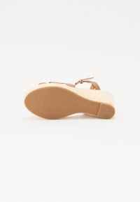 Sandale compensée avec une tige synthétique beige, une bride de cheville et une semelle plateforme en jute texturé. Semelle en caoutchouc plate avec un motif simple.