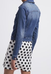 Denimjacka i medelblått, med klassisk krage och figursydd design, tillsammans med en svart kjol med prickar.