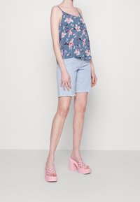 Haut sans manches floral bleu avec des accents rose et violet, associé à un short en denim bleu clair et des sandales à plateforme roses.