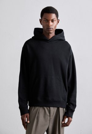 Black cotton hoodie with a front pocket, long sleeves, and a relaxed fit. It features a drawstring hood and ribbed cuffs.