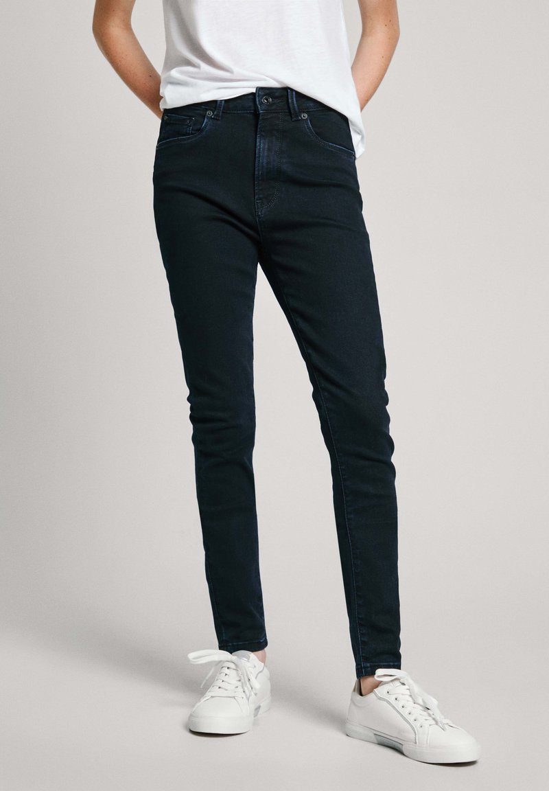 Černé skinny džíny z denimu, s klasickým designem pěti kapes a viditelným šitím. V kombinaci s bílými teniskami.