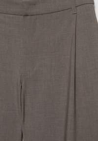 Close-up of brown dress pants showing waistband, side pocket, and front crease details in woven fabric.