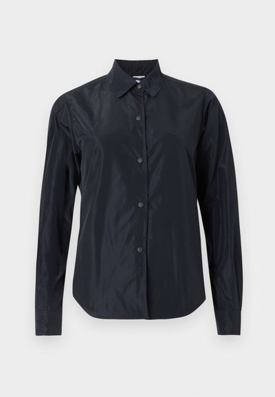 Chemise noire à manches longues avec boutons, col, tissu mat et poignets ajustés, présentée sur un fond clair neutre.