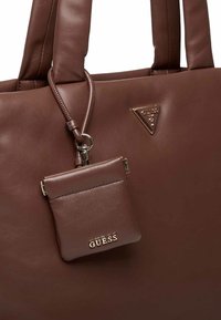 Sac cabas en cuir marron avec poignées arrondies, doté d'une petite pochette attachée. Accents en métal doré et emblème de logo triangulaire.