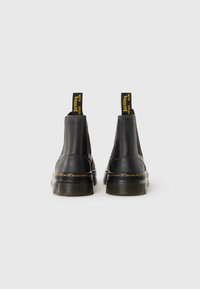 Sorte lær ankle boots med elastiske sidepaneler, kontrasterende gul søm og en gul pull-tab som leser "WITH SOLES Bouncing."