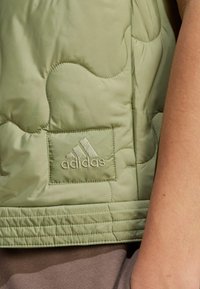 Svetlozelena podložena brezrokavnik s strukturiranim dizajnom, vezenim Adidasovim logotipom na kvadratnem pokrovu in šivanim robom.