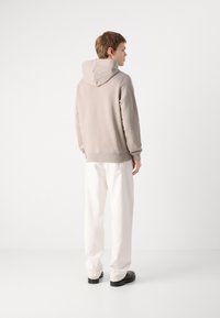 Felpa grigia con cappuccio, dal taglio rilassato, con polsini e orlo a costine, abbinata a pantaloni bianchi larghi e scarpe nere.