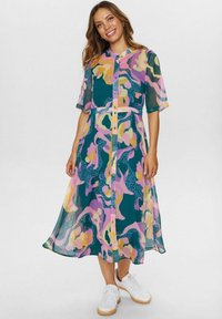 Rochie transparentă, vaporoasă, cu nasturi, având un model abstract colorat în nuanțe de roz, violet și verde. Se asortează cu adidași albi.