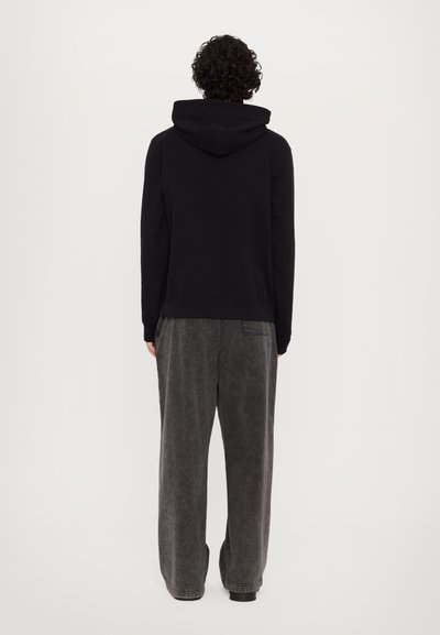 Sweatshirt noir à capuche avec une texture douce, associé à un pantalon gris ample avec une finition délavée et des jambes larges.