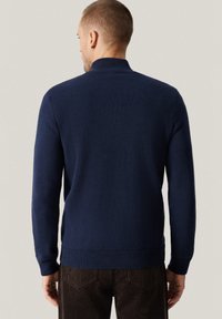 Granatowy dzianinowy sweter z wysokim kołnierzem i prążkowanym dołem. Materiał jest miękki o gładkiej fakturze, dopasowany krój podkreśla talię.