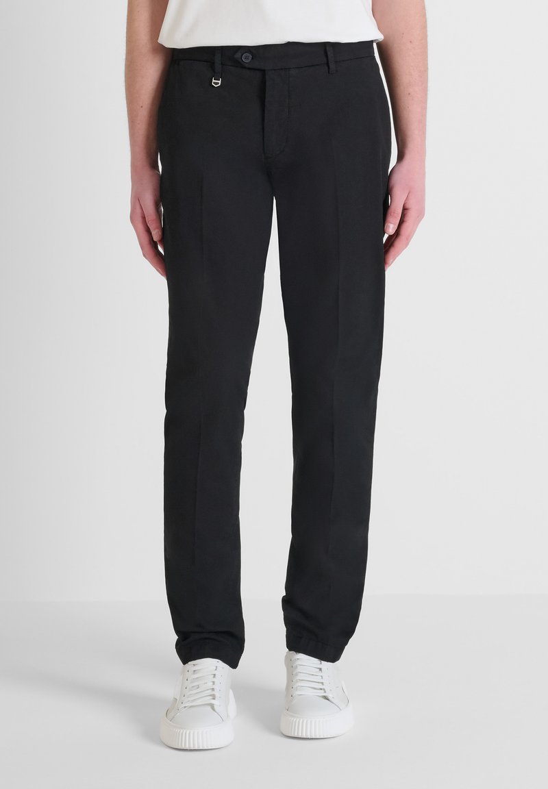Pantalones negros a medida con una textura suave, que cuentan con un ajuste clásico, bolsillos frontales y un pequeño acento de metal cerca de la cintura.