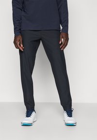Dark gray golf pants with a slim fit, lightweight fabric, and smooth texture, paired with white golf shoes featuring blue accents.