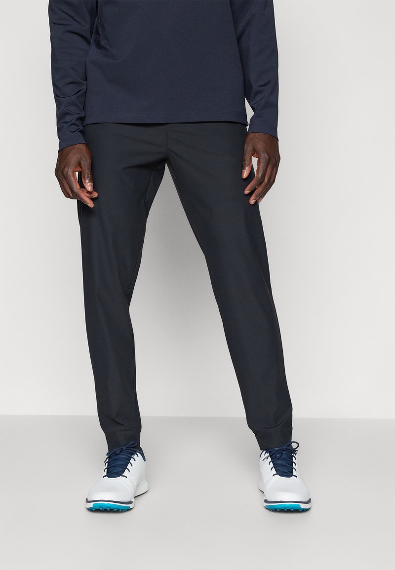 Dark gray golf pants with a slim fit, lightweight fabric, and smooth texture, paired with white golf shoes featuring blue accents.