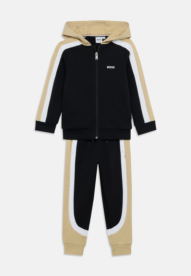 Μαύρο φούτερ με φερμουάρ και μπεζ κουκούλα, λευκές ρίγες στο πλάι και λογότυπο "BOSS". Συντονισμένο μαύρο παντελόνι με μπεζ/λευκές λεπτομέρειες και ριμπ μανσέτες.