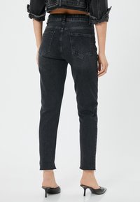 Jeans ajustados de mezclilla negra con una cintura alta, que cuentan con bolsillos traseros, piernas rectas y un dobladillo deshilachado. Combinados con mocasines negros de tacón.