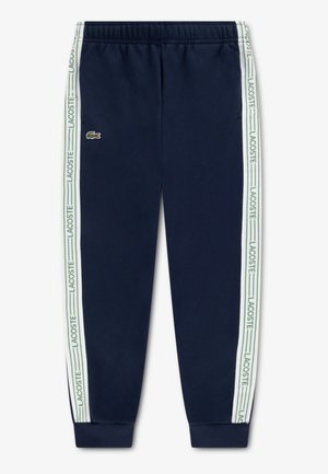 Pantaloni de trening bleumarin din bumbac, cu talie elastică, tivuri strânse și dungi albe cu sigla „LACOSTE” pe laterale.